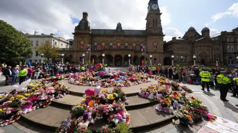 PA Media Flowers and balloons sit in the centre on ground, outside a theatre