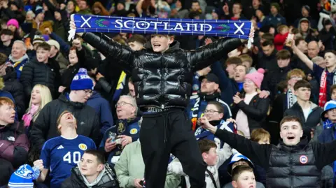 PA Media Fans celebrate in the Scotland stands, including a man dressed in black who holds up a Scotland scarf