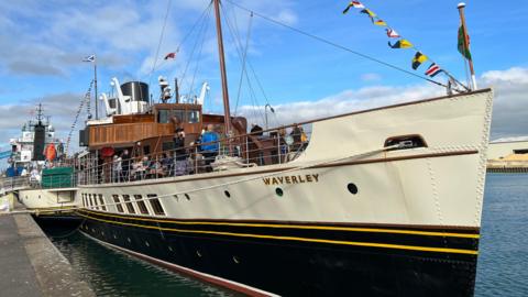 The Waverley stops at Shoreham Port - a large, white, yellow and black ship with wooden cabin and flags