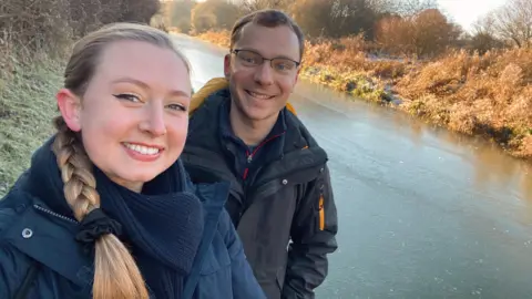 Alexandra Petri Alexandra Petri and Ross Jones wearing winter coats and standing beside a frozen river