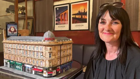 Karen, a woman in her 50s with dark brown hair and glasses on her head, sitting next to the model of Union Corner.