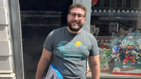 Enrico, 28, stands on a UK high street holding a parcel