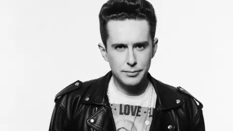 Trevor Leighton Black and white image of singer Holly Johnson, who has short dark hair and is wearing a black leather jacket and a t-shirt with an image of the Virgin Mary and the word Love on it