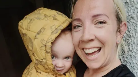 Laura Oakes Laura Oakes, who has blonde hair and wears a running top, smiles at the camera while holding her 11-month-old son