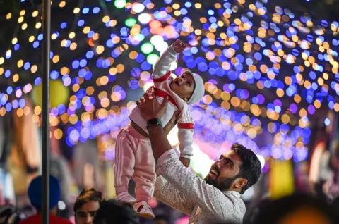 Getty Images A man lifts his child to see the Diwali lights being set up at Janpath Market in New Delhi