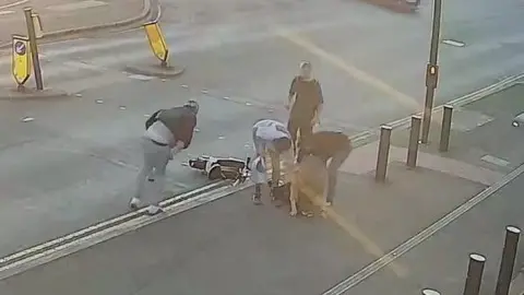 A group of people surround a woman who has been knocked over by an e-bike