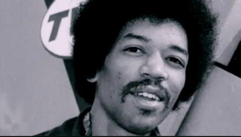 A close-up of the guitarist Jimi Hendrix, who is looking relaxed and smiling at the camera