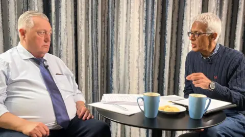 Two men sat opposite each other at a table talking to each other