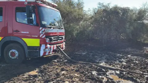 Paul McNulty The front of a fire engine with a tow rope attached, stuck in heavy mud