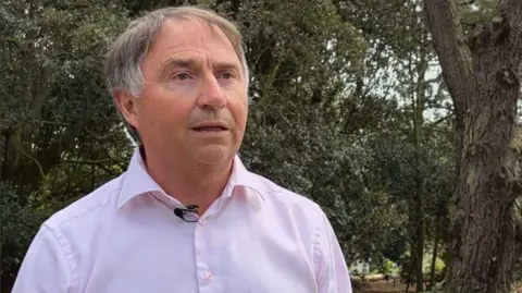 BBC Association of Guernsey Charities chair Wayne Bulpitt. he has short grey hair and is wearing a pink shirt. 