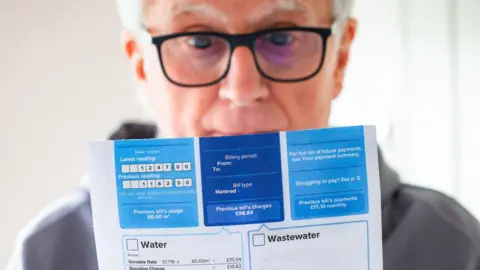 Getty Images An old man looks at a water bill. 