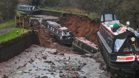 PA Media Two canal boats at the bottom of a muddy hole and a third hanging over the edge