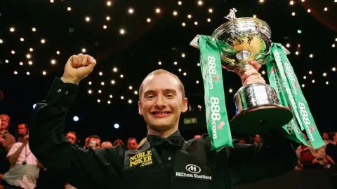 Getty Images Graeme Dott after winning the world snooker championship in 2006. He is holding his trophy in the air. It is silver and has green ribbons attached.