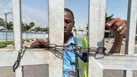 A worker stands by the gate of the domestic airport, which has been chained to prevent passengers from entering the premises, as Nigeria's main labour unions called for an indefinite strike from Monday after failing to agree to a new minimum wage with the government, in Lagos, Nigeria, 3 June 2024