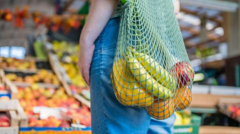 A string bag full of fruit and vegetables and with a market stall visible in the background