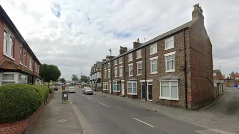 Google Maps An image of a street with houses on each side. Two cars are travelling in opposite directions of the road.