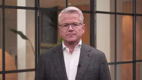 Maersk chief executive Vincent Clerc wears a white shirt, brown suit jacket and glasses as he speaks to the BBC. 