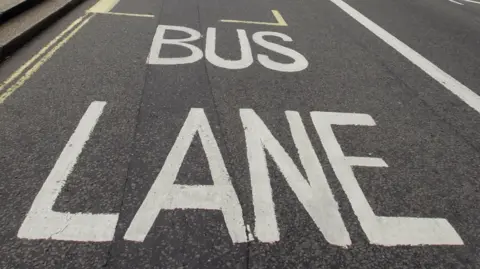 A bus lane sign painted in white on a tarmac road