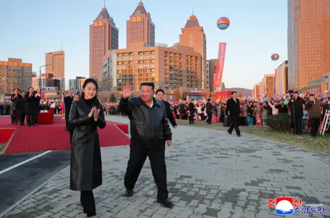 KCNA VIA KNS via AFP This picture taken on February 16, 2026 and released by North Korea's official Korean Central News Agency (KCNA) on February 17, 2026 shows North Korean leader Kim Jong Un (C) and his daughter Ju Ae (L) responding to citizens at the inauguration ceremony of 10,000 flats at fourth stage in Hwasong area of Pyongyang. 
