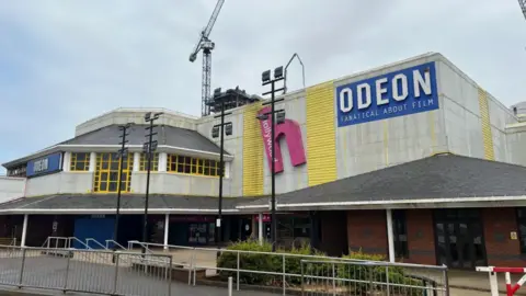 A general view of the Odeon cinema site, with a blue Odeon sign that says "fanantical about film" underneath it". A pink Hollywood Bowl logo is next to it.