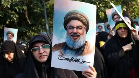 Getty Images Iranian women hold a photo of Hezbollah leader Hassan Nasrallah, who was killed in an Israeli airstrike on the southern suburbs of Beirut on September 27.