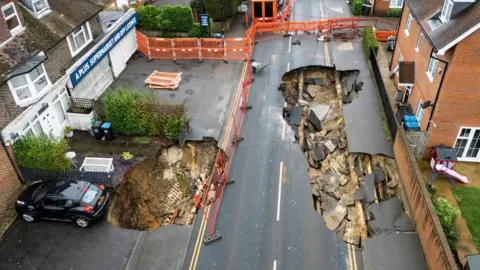 EPA-EFE/REX/Shutterstock An aerial photograph of a road with two large sinkholes in. Orange fences surround the sinkholes.