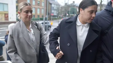 PA Media Kristie Mewis and Sam Kerr holding hands and arriving at court. Both are dressed smartly.