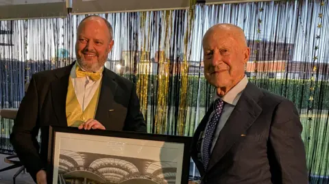 WTW Lord Foster smiles at the camera as he is presented with a photo of the interior of the building's entrance.