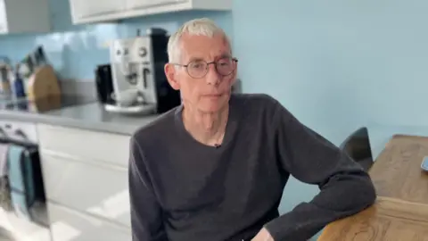 BBC Paul Gosling sits at a wooden table in a blue kitchen