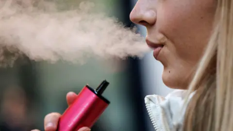 A woman using a single-use vaping product. She has blonde hair and is blowing out a plume of smoke which she has taken in from a pink vape.