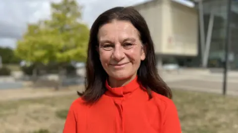 Steve Hubbard/BBC Ms Smith is smiling at the camera from outside the council office building. She wears a bright burnt orange colour top and has shoulder length brown hair. 