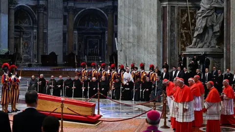 Swiss guards and members of the clergy (Top R) stand next to the coffin of the late Pope Francis inside St Peter's Basilica