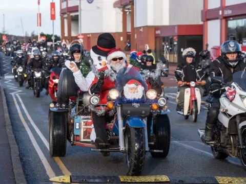 Ian Knight / Z70 Photography A group of bikers set off on a charity motorcycle ride. Featured is a man dressed as Santa on a three-wheeled bike with a passenger dressed as a snowman.