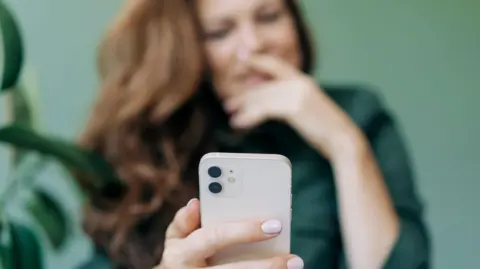 Getty Images Woman out of focus holding a white iPhone