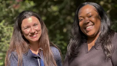 Iona Tsonkov on the left of the picture and Serona Constance who's on the right are standing closely together in the garden of Don Way's retirement complex. Bathed in sunlight they're both smiling at the camera. 