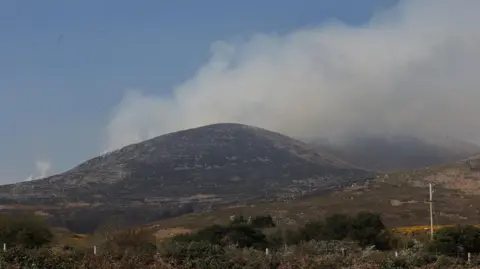 PA Media Smoke billowing out into the air behind a mountain. 