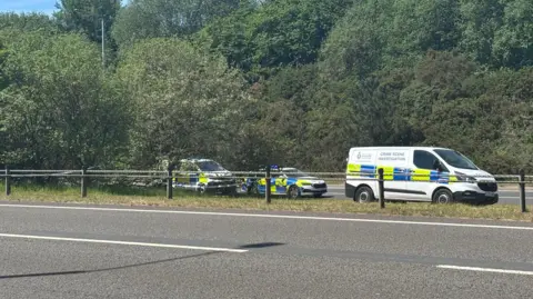 A crime scene investigation van and two police cars and cones are parked as they investigate an incident.