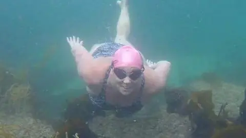Lindsey Walke A swimmer in a pink swim hat and wearing goggles under water.