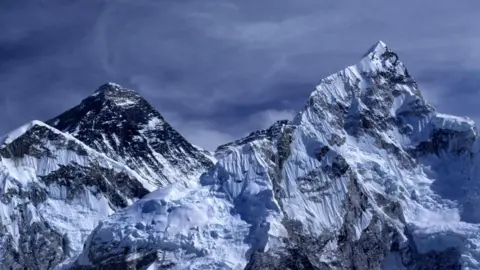 Getty Images Mount Everest. Two mountain peaks covered in snow. The sky is dark blue and it looks stormy. 