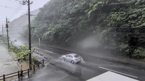 A car makes its way through strong winds and rain as Typhoon Dolphin approaches, in Nazeasahicho, Amami, Kagoshima, Japan, August 7, 2026, in this screengrab obtained from a social media video. 