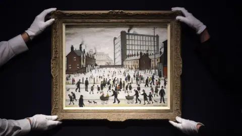 Getty Images Two people in white gloves hold LS Lowry's artwork, The Mill, Pendlebury, which depicts a crowd of people in front of terraced houses and a mill