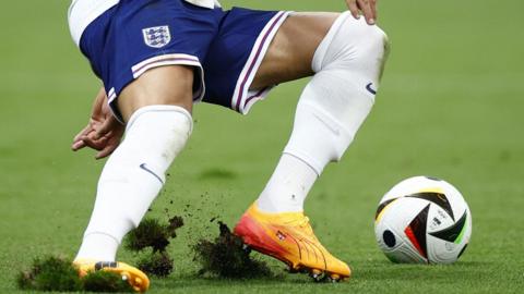 A player cuts up the grass with his boots as he turns to the ball