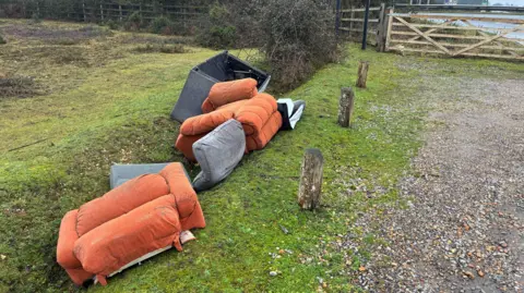 A tatty sofa and chair cushions by the side of a road in the New Forest. The cushions and sofa covers are orange and grey in colour.
