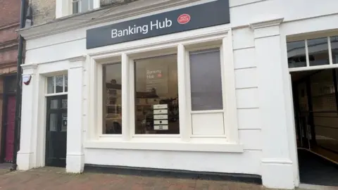 A former HSBC bank building converted into a banking hub with white rendered walls, a black door and signs saying banking hub.