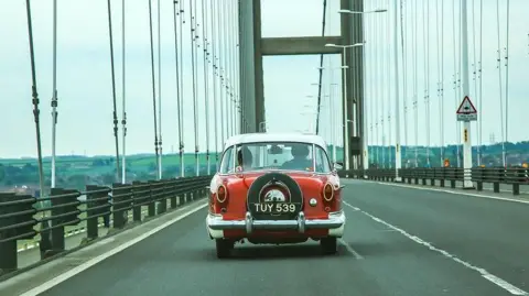 A vintage red car travelling across the Humber Bridge 