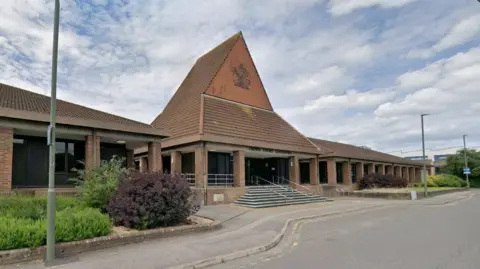 The outside of Guildford Crown Court, a red brick building with steps leading up to it. It has a large triangle shaped roof.