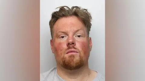 Northamptonshire Police A police custody of Paul Knight in a grey top looking at the camera. He has red cheeks, has freckles, ad a goatee ginger-brown beard.