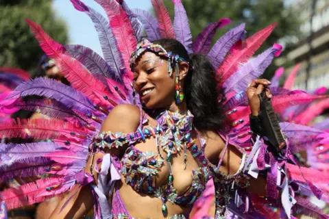 Alishia Abodunde / Getty Images A woman dances during a parade at the Notting Hill Carnival