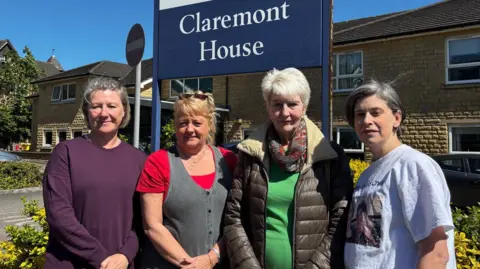 Four women stood in front of a red brick, two-storey care home. There is a blue sign indicating it is Claremont House.
