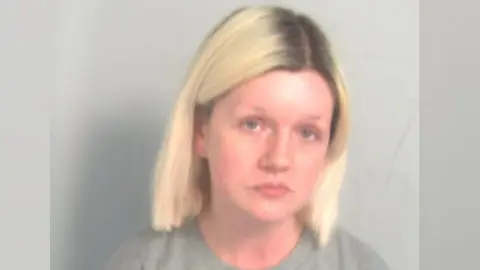 Essex Police Custody mugshot of Virginia McCullough. She has airy  blond hairsbreadth  with acheronian  roots. She is wearing a grey sweater and is looking solemnly astatine  the camera.